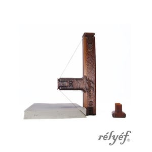 Puede incluir: Una herramienta de madera marrón con un alambre, una pequeña base rectangular y una pequeña pieza separada. La herramienta tiene el texto "30" y "45". La palabra "rélyéf" está escrita en una fuente cursiva.