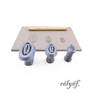 Könnte beinhalten: Ein Set grauer Tonstempel mit ovalem Design, zusammen mit einer Holzrolle und einer Tonplatte. Die Stempel sind in verschiedenen Größen und Formen. Das Wort "rélyéf" ist in grauer Schrift gedruckt.