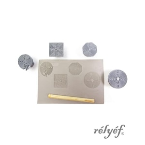 May include: A set of gray labyrinth stamps in various geometric shapes, including circles, squares, and octagons. A wooden rolling pin and a gray rectangular pad are also present. The word "rélyéf" is printed in gray.