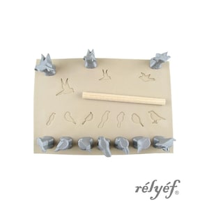 May include: A tan rectangular leather sheet featuring multiple bird-shaped indentations, accompanied by ten grey 3D-printed bird stamps and a single wooden dowel. The word "rélyéf" is printed in the bottom right corner of the image.