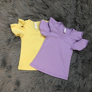 May include: Two short-sleeved shirts with ruffled sleeves. One shirt is yellow and the other is purple.