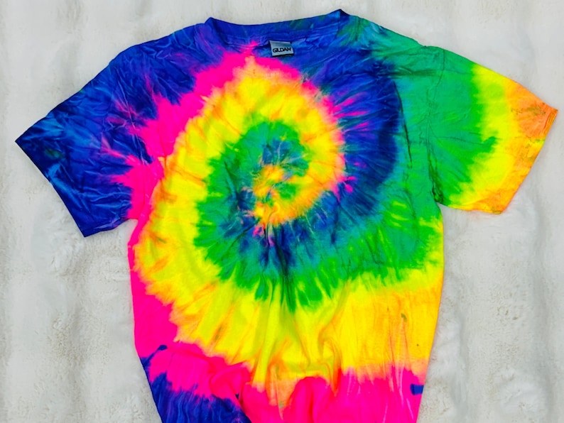 May include: A tie-dye t-shirt with a bright yellow, green, blue, and pink spiral design. The shirt has short sleeves and a crew neck.