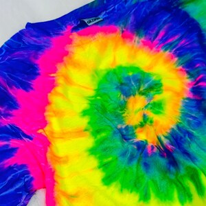 May include: A tie-dye shirt with a bright yellow, green, blue, and pink spiral pattern. The shirt has a tag that says "Gildan" on it.