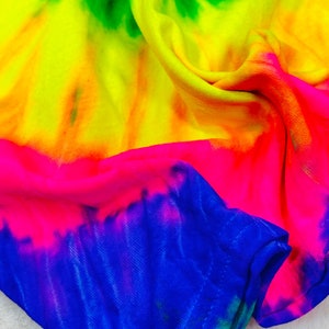 May include: A tie-dye fabric with a bright yellow, orange, pink, blue and green color scheme. The fabric is folded and draped, showing the different colors.