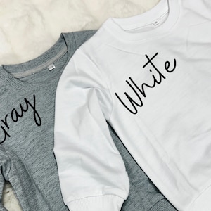 May include: Two long-sleeved shirts, one grey with the word "Gray" written on it, and one white with the word "White" written on it.