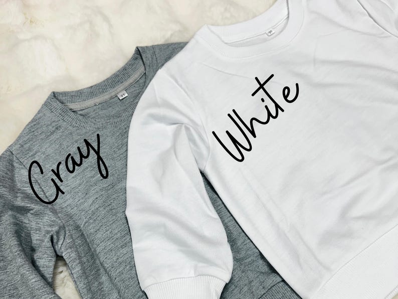 May include: Two long-sleeved shirts, one grey with the word "Gray" written on it, and one white with the word "White" written on it.