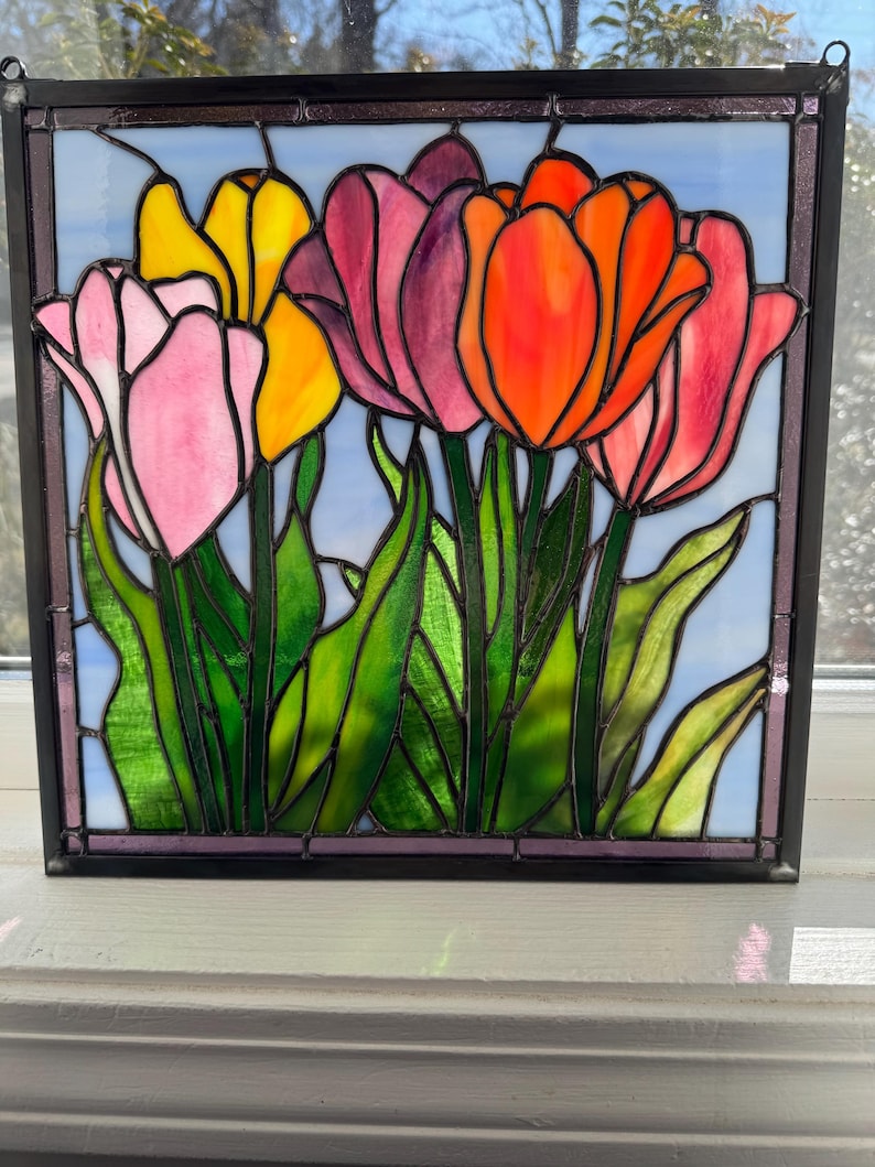 May include: A stained glass window depicting a bouquet of colorful tulips with green leaves against a light blue background.