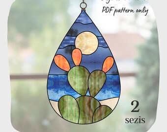 May include: A stained glass pattern of a cactus with a blue sky and a yellow sun in the background. The pattern is in the shape of a teardrop and is labeled "2 sezis".
