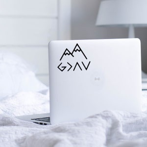 May include: A black and white sticker with a mountain range design and the text "God is greater than the highs and lows". The sticker is on a white laptop.