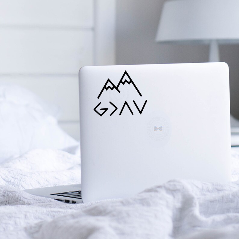 May include: A black and white sticker with a mountain range design and the text "God is greater than the highs and lows". The sticker is on a white laptop.