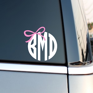 May include: White monogram decal with a pink bow on a black car window. The monogram reads "BMD".