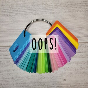 May include: A color swatch fan with a variety of colors, including blue, green, pink, purple, and orange. The fan is held together by a silver ring. The word "OOPS!" is written across the center of the fan.