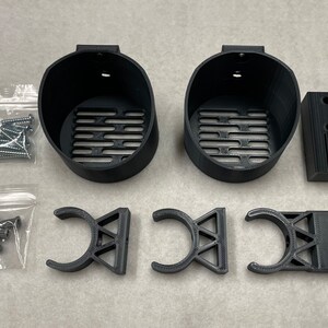 May include: A collection of black 3D-printed mounting hardware components, including two circular holders with slotted bases, three curved brackets, and a rectangular block. Also included are two small bags of screws and anchors.
