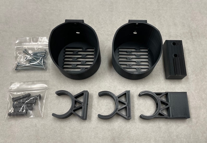 May include: A collection of black 3D-printed mounting hardware components, including two circular holders with slotted bases, three curved brackets, and a rectangular block. Also included are two small bags of screws and anchors.