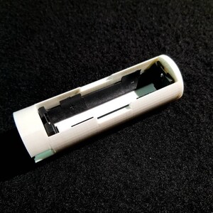 May include: A white, cylindrical object with a rectangular opening, revealing a black interior and small green accents. The object appears to be a component or housing for an electronic device, possibly a battery holder.
