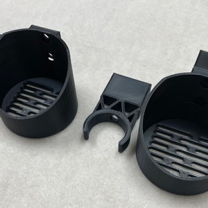 May include: Black 3D-printed cup holders with a slotted base and a clip-on design. The holders have a cylindrical shape with a small handle on the side. The set includes two cup holders and two clip-on attachments.
