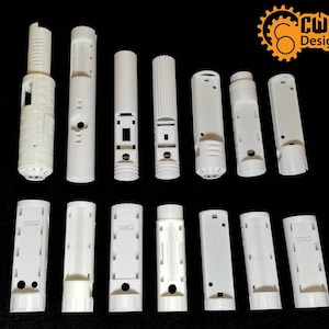 May include: A collection of white 3D-printed parts, possibly for a larger assembly, arranged on a black surface. The parts vary in shape and size, including cylindrical and rectangular components. The logo "CWS Designs" is visible in the upper right corner.