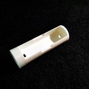 May include: A white, rectangular, 3D-printed object with a hollow interior and a small rectangular cutout. The object has a rounded end and is set against a black background.