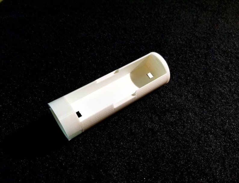 May include: A white, rectangular, 3D-printed object with a hollow interior and a small rectangular cutout. The object has a rounded end and is set against a black background.