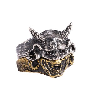 Puede incluir: Un anillo de plata y oro con una m&aacute;scara oni tridimensional detallada con cuernos y colmillos.
