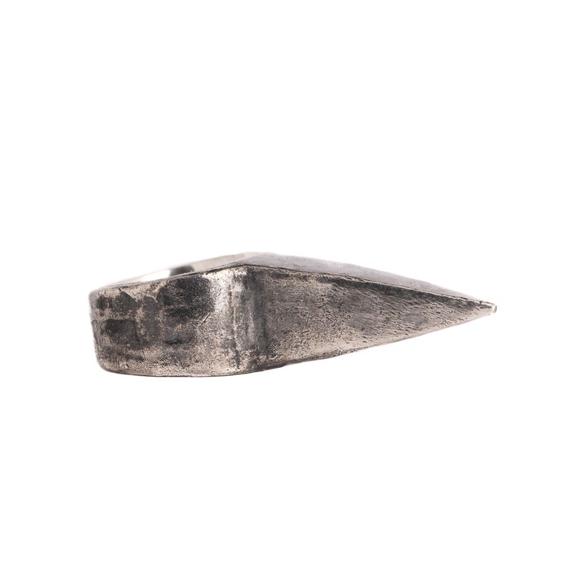 May include: A silver ring with a pointed, triangular design. The ring has a textured surface and a worn look.