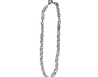 Può includere: Collana color argento con un design a catena strutturata. La collana presenta una chiusura a toggle ed è esposta su uno sfondo bianco. Le maglie della catena hanno una forma irregolare e organica, aggiungendo interesse visivo al gioiello.