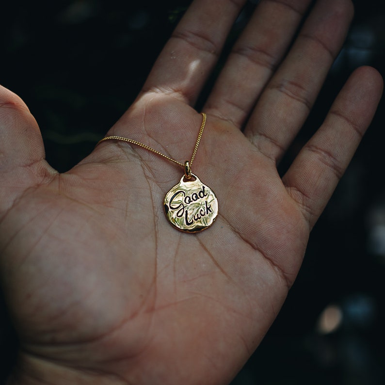 May include: A gold necklace with a round pendant that says "Good Luck" in cursive.