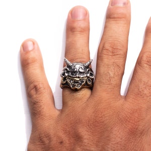 Puede incluir: Un anillo de plata y oro con un dise&ntilde;o detallado de la cara de un demonio. El anillo se lleva en el dedo de una persona.