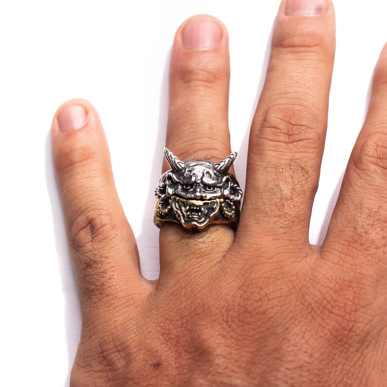 Puede incluir: Un anillo de plata y oro con un dise&ntilde;o detallado de la cara de un demonio. El anillo se lleva en el dedo de una persona.