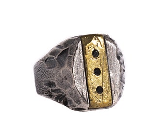 May include: A silver and gold ring with a textured surface and three black gemstones set in a gold band.