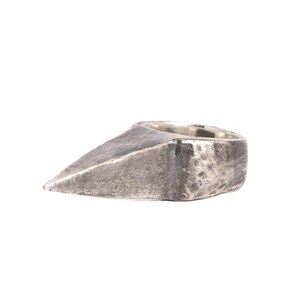 May include: A silver ring with a pointed, triangular design. The ring has a textured, worn finish.