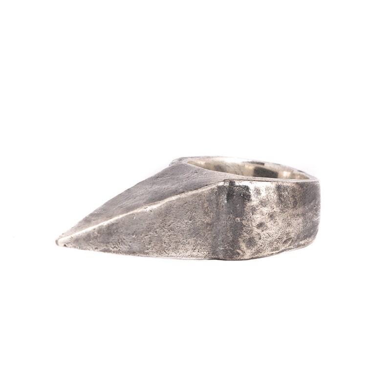 May include: A silver ring with a pointed, triangular design. The ring has a textured, worn finish.