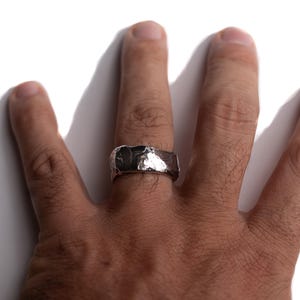 Puede incluir: Un anillo de plata con textura martillada. El anillo es ancho y tiene una parte superior plana.
