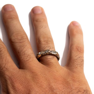 May include: A gold ring with a textured, organic design. The ring is worn on a person's finger.