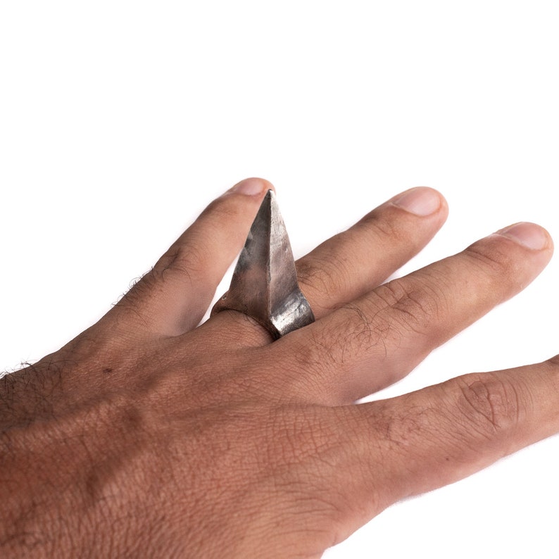 May include: A silver ring with a sharp, triangular point. The ring is worn on a person's finger.