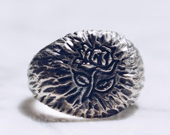 May include: A silver ring with a textured surface and a raised rose design.