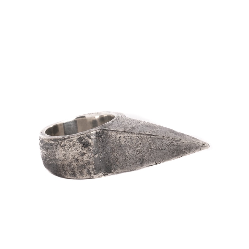 May include: A silver ring with a pointed, triangular design. The ring has a textured, worn finish.