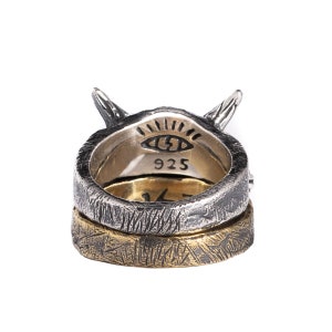 Puede incluir: Un anillo de plata con una banda de oro, que presenta un dise&ntilde;o de ojo estilizado y la inscripci&oacute;n "925". El anillo tiene una superficie texturizada y un par de cuernos en la parte superior.