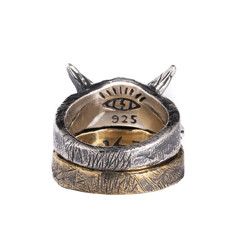 Puede incluir: Un anillo de plata con una banda de oro, que presenta un dise&ntilde;o de ojo estilizado y la inscripci&oacute;n "925". El anillo tiene una superficie texturizada y un par de cuernos en la parte superior.
