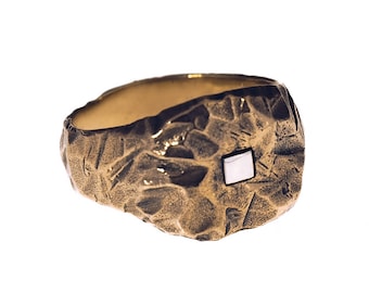 May include: A gold ring with a textured surface and a small square-shaped stone set in the center.
