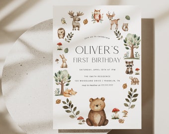 May include: A woodland-themed first birthday invitation with a brown bear, a raccoon, a deer, a moose, a fox, a hedgehog, a bird, a rabbit, a turtle, and a snail. The invitation is decorated with leaves, mushrooms, and acorns. The text on the invitation reads "Join us to celebrate Oliver's First Birthday. Saturday, April 10th at 1 pm. The Smith Residence. 123 Woodland Drive | Franklin, TN. rsvp to Heather at 777.777.7777."