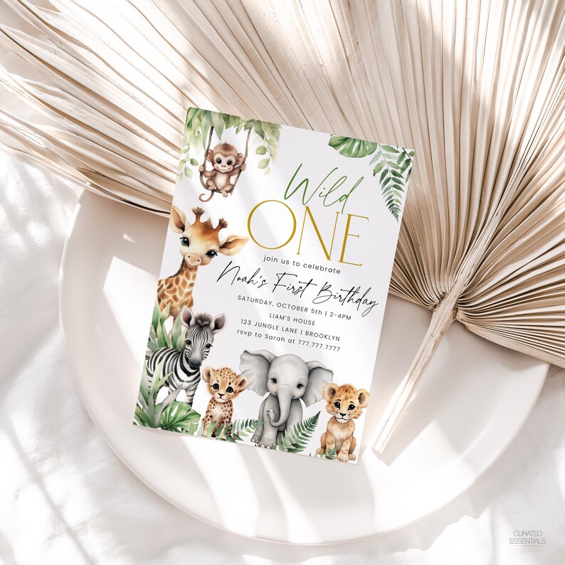 May include: A white invitation card with a jungle theme, featuring illustrations of a giraffe, zebra, lion, cheetah, elephant, and monkey. The text reads "Wild One" and "Noah's First Birthday". The card is decorated with green foliage.