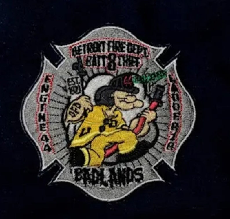 May include: A gray and red embroidered patch with a cartoon firefighter holding a hose. The patch says "Detroit Fire Dept. Batt. 8 Chief Engine 44 Ladder 78  Brdlands" and "Est. 1900".