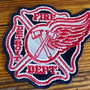 Puede incluir: Un parche bordado azul y rojo con las palabras "Detroit Fire Dept." y un ala roja con detalles blancos.