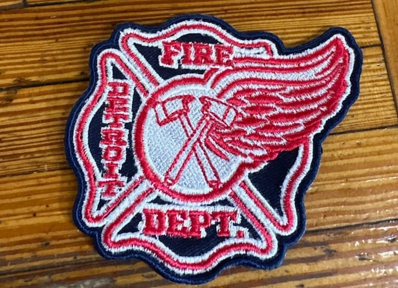 May include: A blue and red embroidered patch with the words "Detroit Fire Dept." and a red wing with white accents.