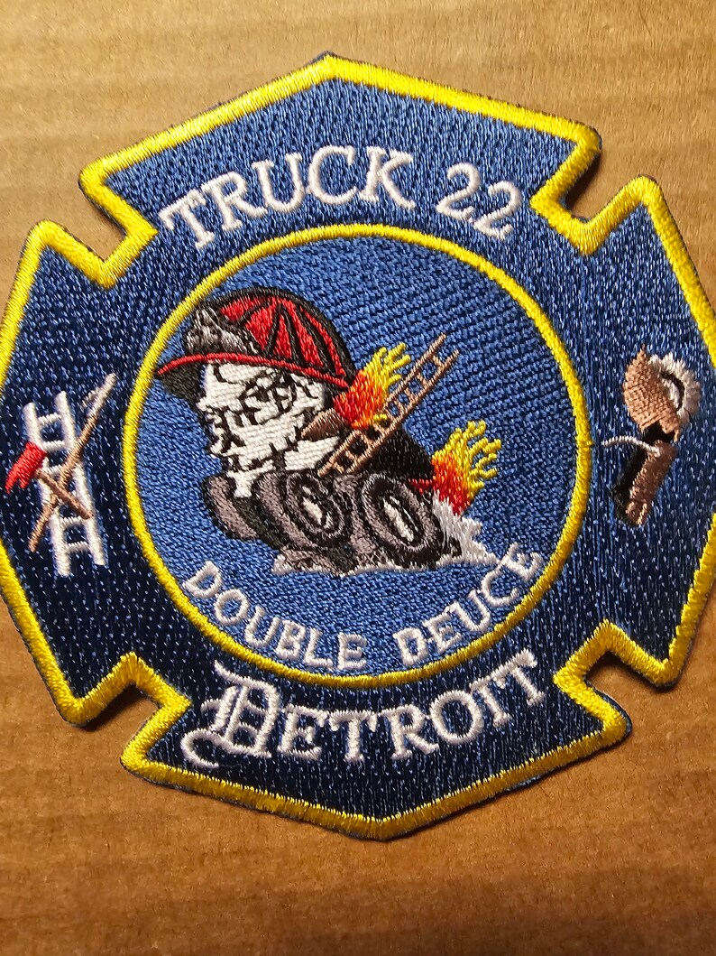 May include: A blue and yellow firefighter patch with the text "TRUCK 22 DOUBLE DEUCE DETROIT" and a cartoon image of a firefighter.