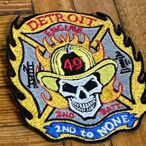 May include: A yellow and black embroidered patch with a skull and crossbones. The patch reads "Detroit Engine 49 2nd to None".