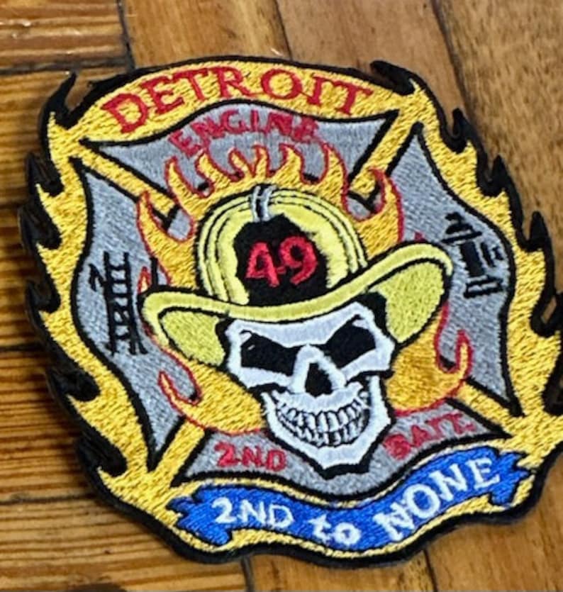 May include: A yellow and black embroidered patch with a skull and crossbones. The patch reads "Detroit Engine 49 2nd to None".