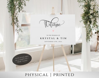 May include: White wedding welcome sign with black calligraphy text that reads "Welcome" with a pink heart above the text. The sign also includes the text "To the wedding of Krystal & Tim September 5th, 2021".