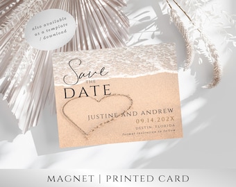 May include: Save the Date magnet with a beach theme. The magnet features a heart drawn in the sand with the text "Save the Date", "Justine and Andrew", "09.14.202X", "Destin, Florida", and "formal invitation to follow".